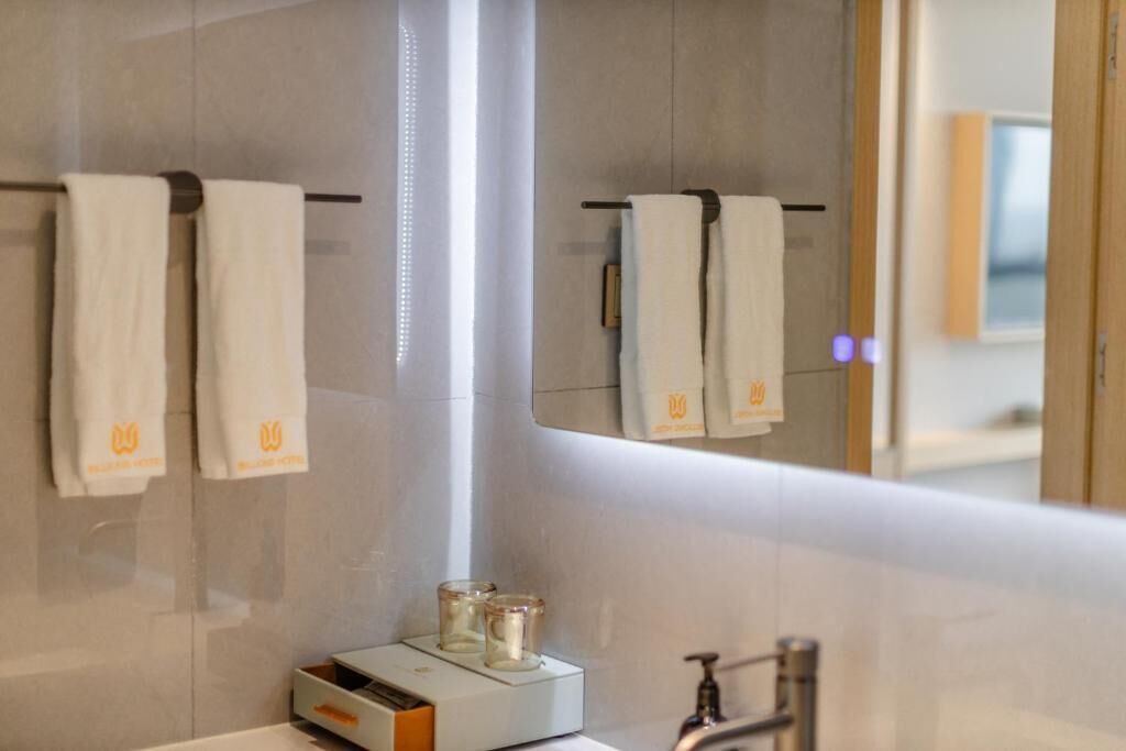 Une salle de bain avec un miroir, deux serviettes suspendues à un porte-serviettes et un distributeur de savon sur le lavabo.