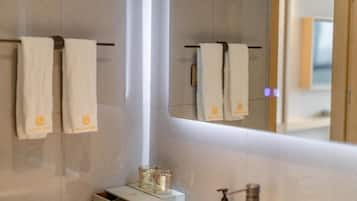 Une salle de bain avec un miroir, deux serviettes suspendues à un porte-serviettes et un distributeur de savon sur le lavabo.
