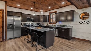 Una cocina moderna con armarios oscuros, una isla central con taburetes, electrodomésticos de acero inoxidable y techo de madera.