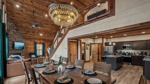 Un comedor amplio con una mesa de madera preparada para seis personas, un candelabro y una escalera que conduce a un nivel superior.