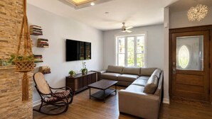 A living room with a sofa, a coffee table, a rocking chair, a TV mounted on the wall, and a bookshelf.