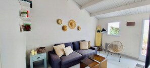 Ein Wohnzimmer mit einer Couch, einem kleinen Tisch, einem Ventilator und einem Surfbrett an der Wand.