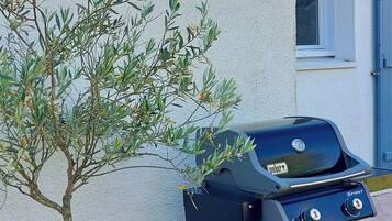 Un barbecue, un arbre en pot et un bâtiment avec un toit en tuiles.