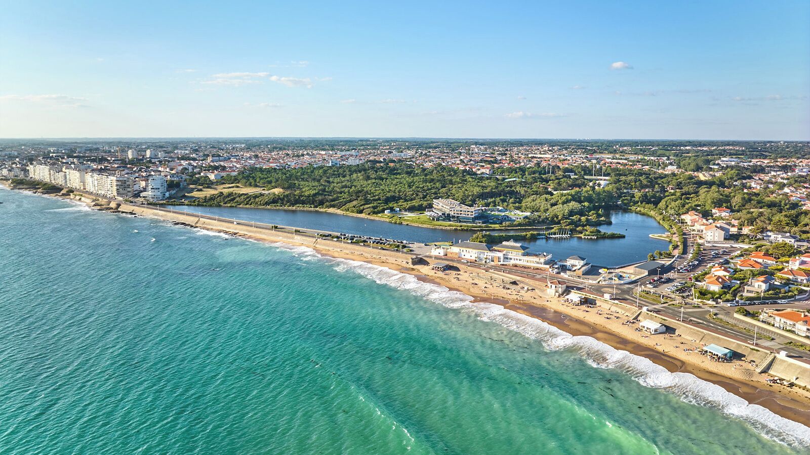 Vista aerea di una città costiera con spiaggia, un porto turistico e zone residenziali.