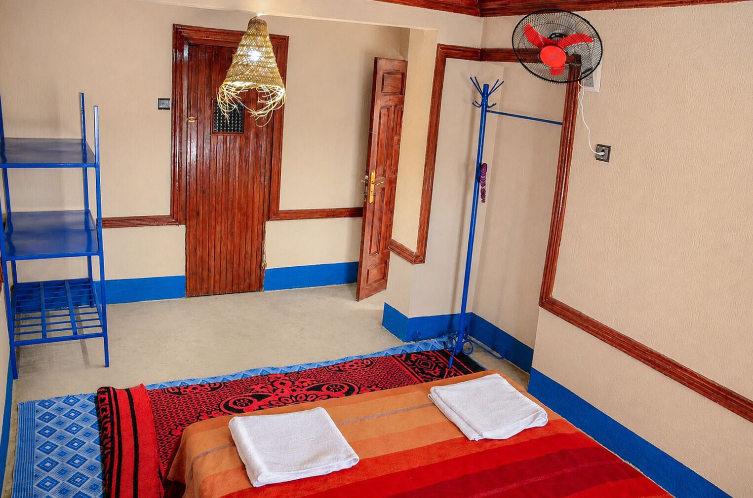 Een kamer met een bed, een blauwe stoel, een ventilator en een deur.