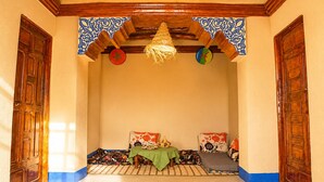 Una habitación con techo de madera alto, una lámpara de fibra trenzada, dos puertas y una cama con manta verde.