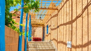 Una escalera exterior techada que conduce a un edificio con una pérgola de madera y un paño rojo en los escalones.