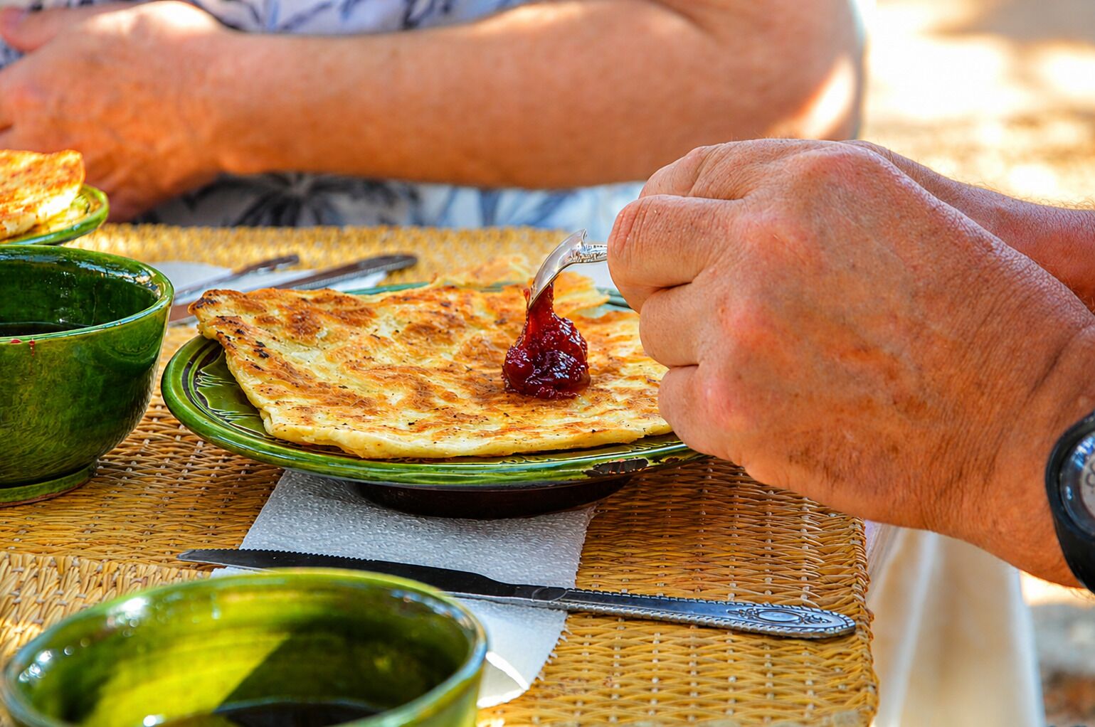 Une personne mange une galette avec de la confiture, sur un set de table en fibres tressées.
