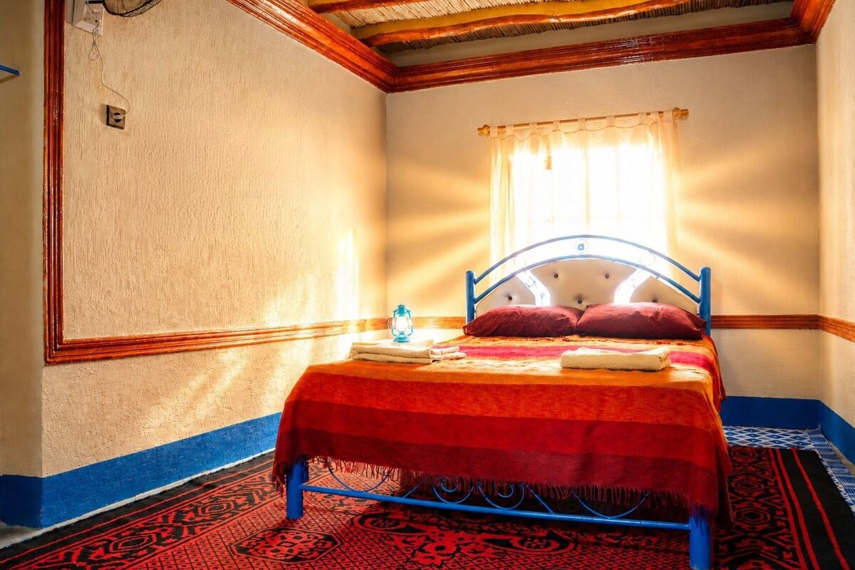 Ein Zimmer mit Bett, einem Vorhangfenster, einem gemusterten Teppich und einer Steckdose.