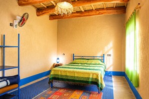 Une pièce avec un lit, une échelle en métal bleue, une petite table avec une lanterne et un tapis à motifs.