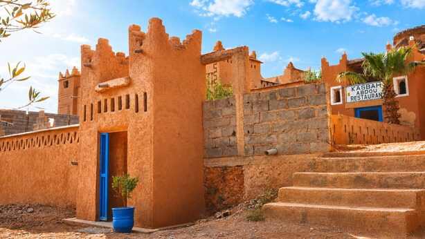 Un edificio tradicional con una puerta azul, un letrero que dice 'Kasbah Abdou Restaurant' y una palmera.
