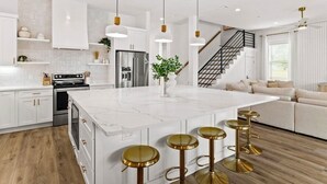 A modern kitchen with white cabinetry, a marble island, and gold bar stools. - Black Pearl | Steps to Beach | Heated Pool & Spa | Free Golf Cart | Game Rooms (Destin)