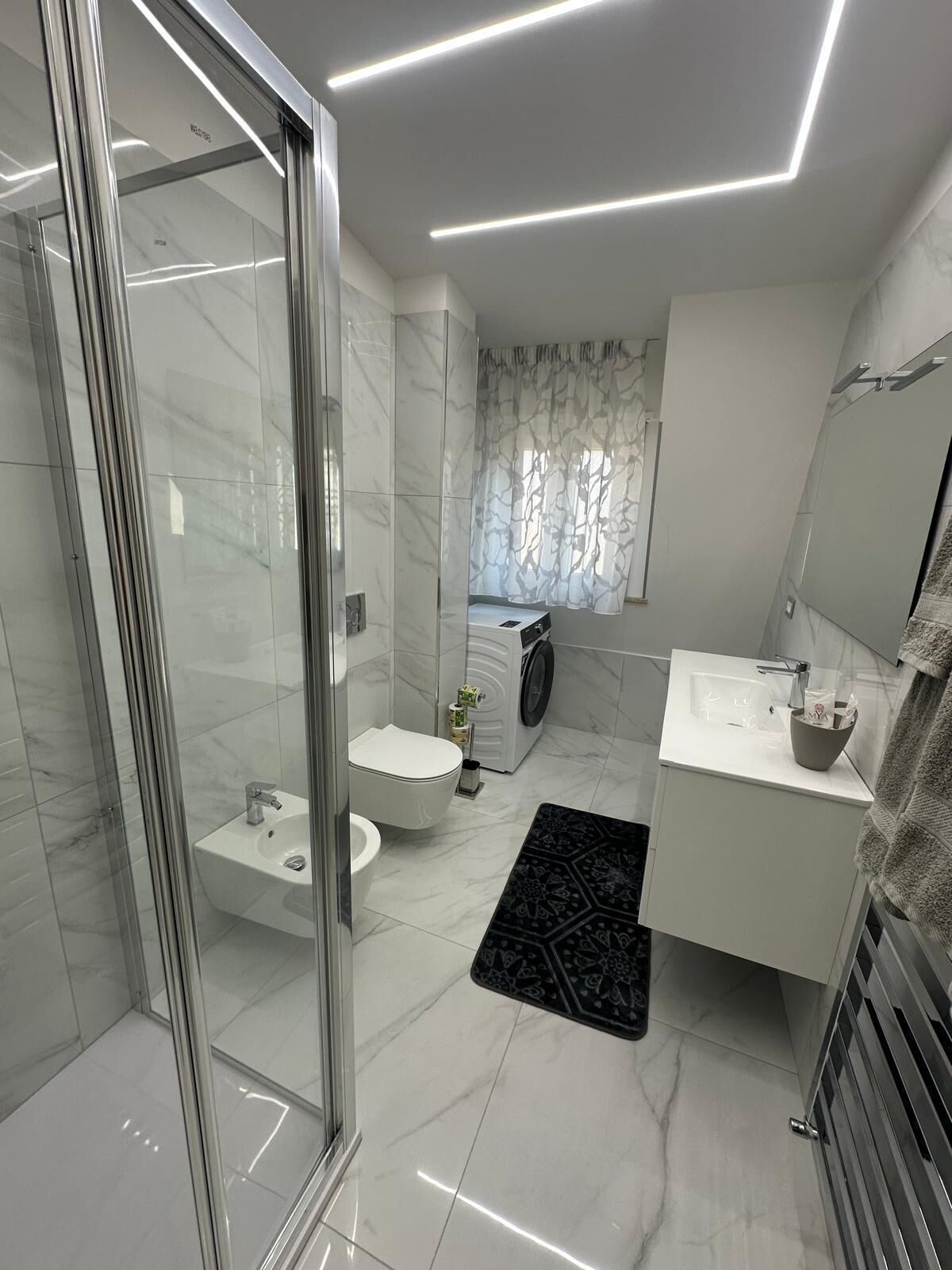 Een moderne badkamer met een douchecabine van glas, een toilet, een bidet, een wasmachine en een wastafel met een handdoekhouder.
