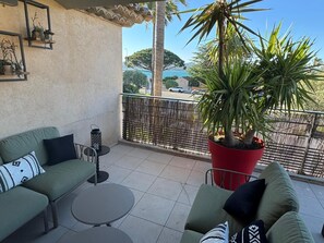 A balcony with a green sofa, a round table, a potted plant, and a view of a street and mountains.