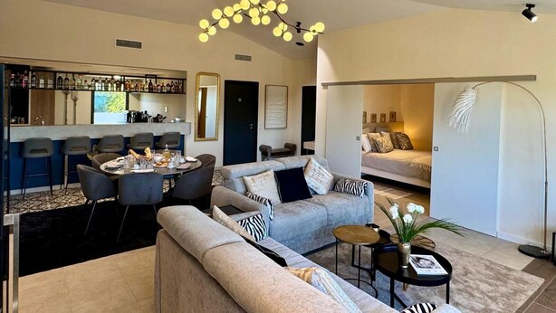 A modern living room with a sofa, coffee table, and a dining area with chairs and a bar. - Roméo Loft Prestige House with Ocean Views on the Outskirts of Saint-Tropez (Gassin)