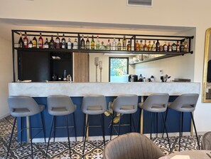 A bar area with a variety of liquor bottles, bar stools, and a kitchen in the background.