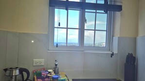 A kitchen with a kettle, a basket of snacks, a bottle, and a window with a view.
