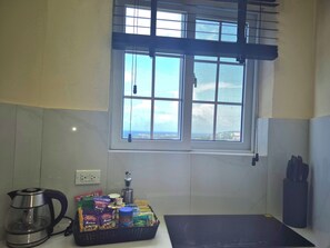 A kitchen with a kettle, a basket of snacks, a bottle, and a window with a view. - Cozy Studio Guests Suite in Runaway Bay (Runaway Bay)