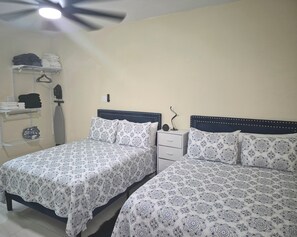 A bedroom with two beds, a bedside table, a hanging rack, and a ceiling fan.