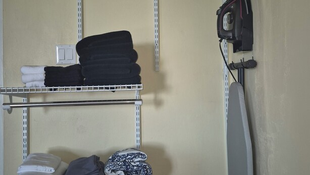 A laundry area with shelves holding folded clothes, a hanging rack, and an ironing board.