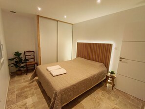 A bedroom with a bed, a chair, a small table with a plant, and a wardrobe. - Beautiful villa with a pool—sleeps 8—Sérignan (Sérignan)