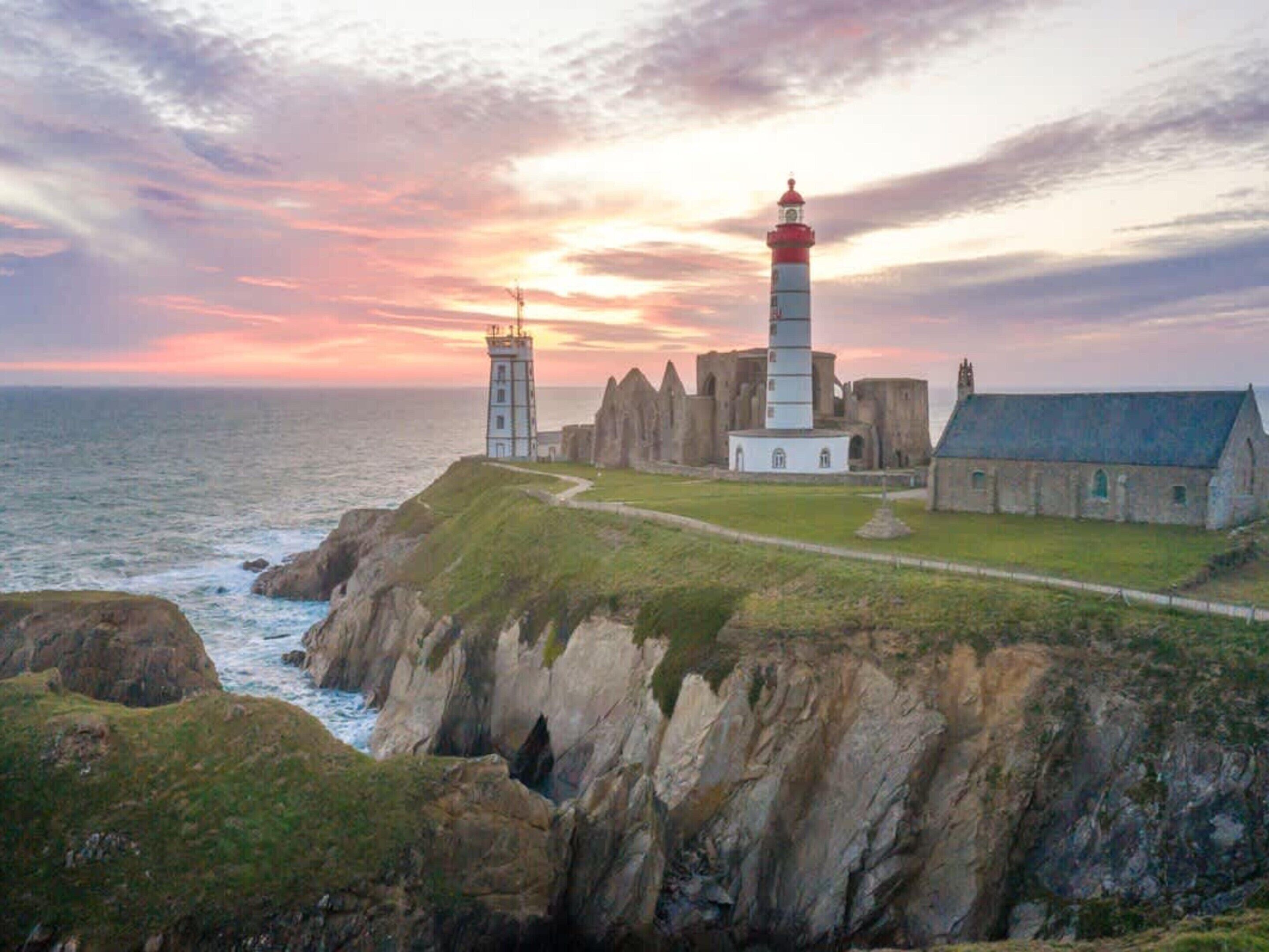 Un phare côtier doté d’une tour et de bâtiments adjacents, entouré de falaises rocheuses et bordé par la mer.