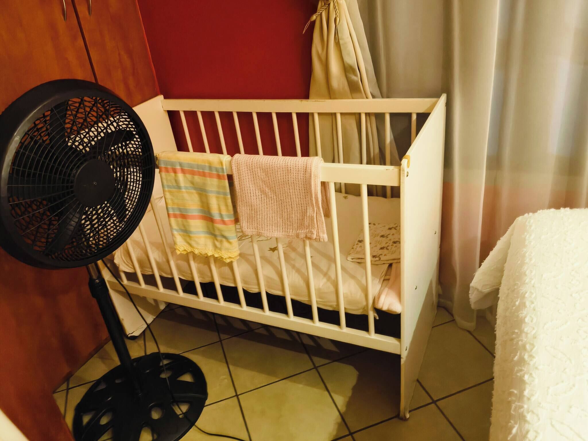 A crib with a fan, a striped blanket, and a plain blanket.