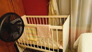 A crib with a fan, a striped blanket, and a plain blanket.