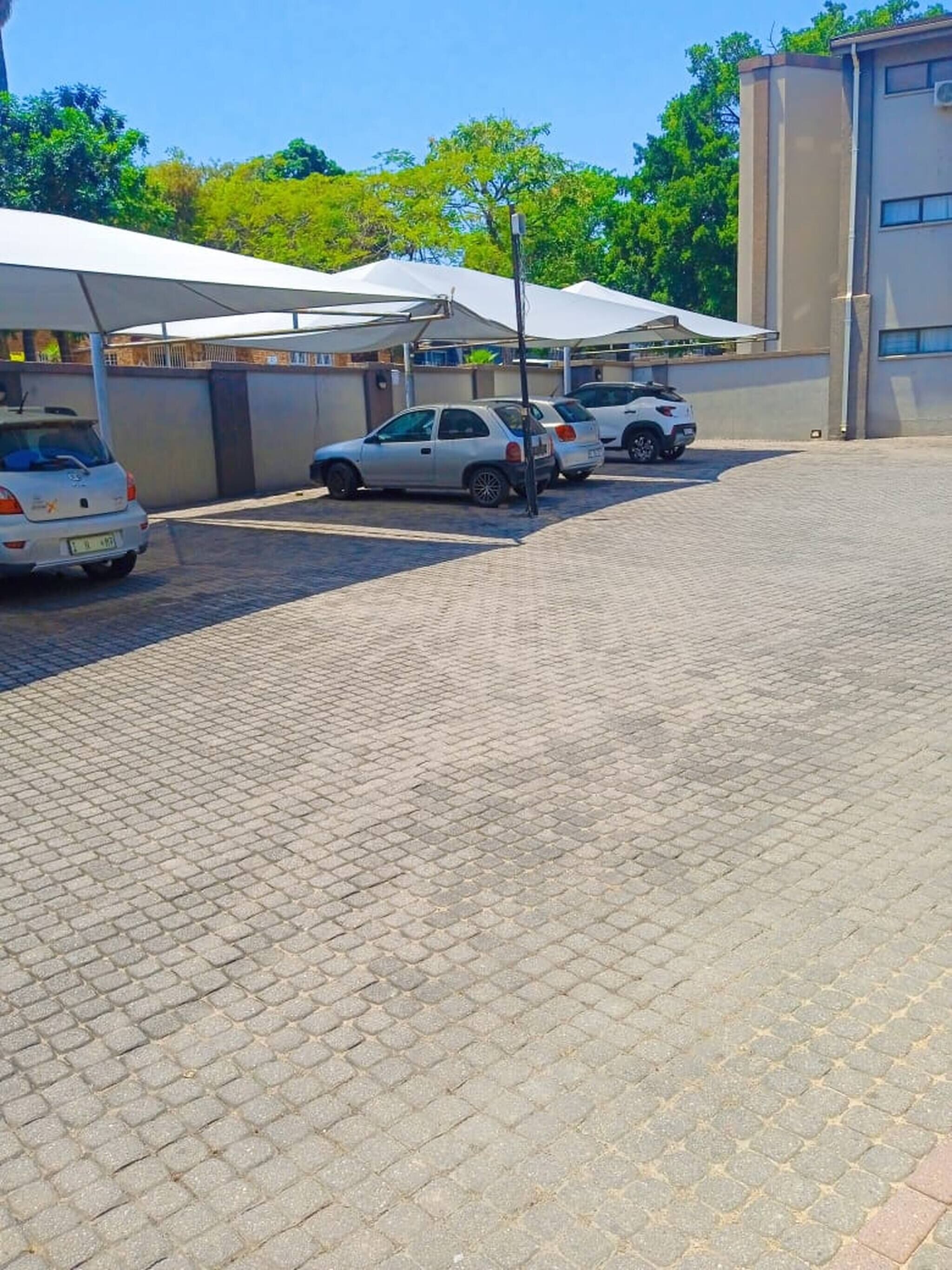 A parking area with cars, a paved surface, and a building with a flat roof in the background.