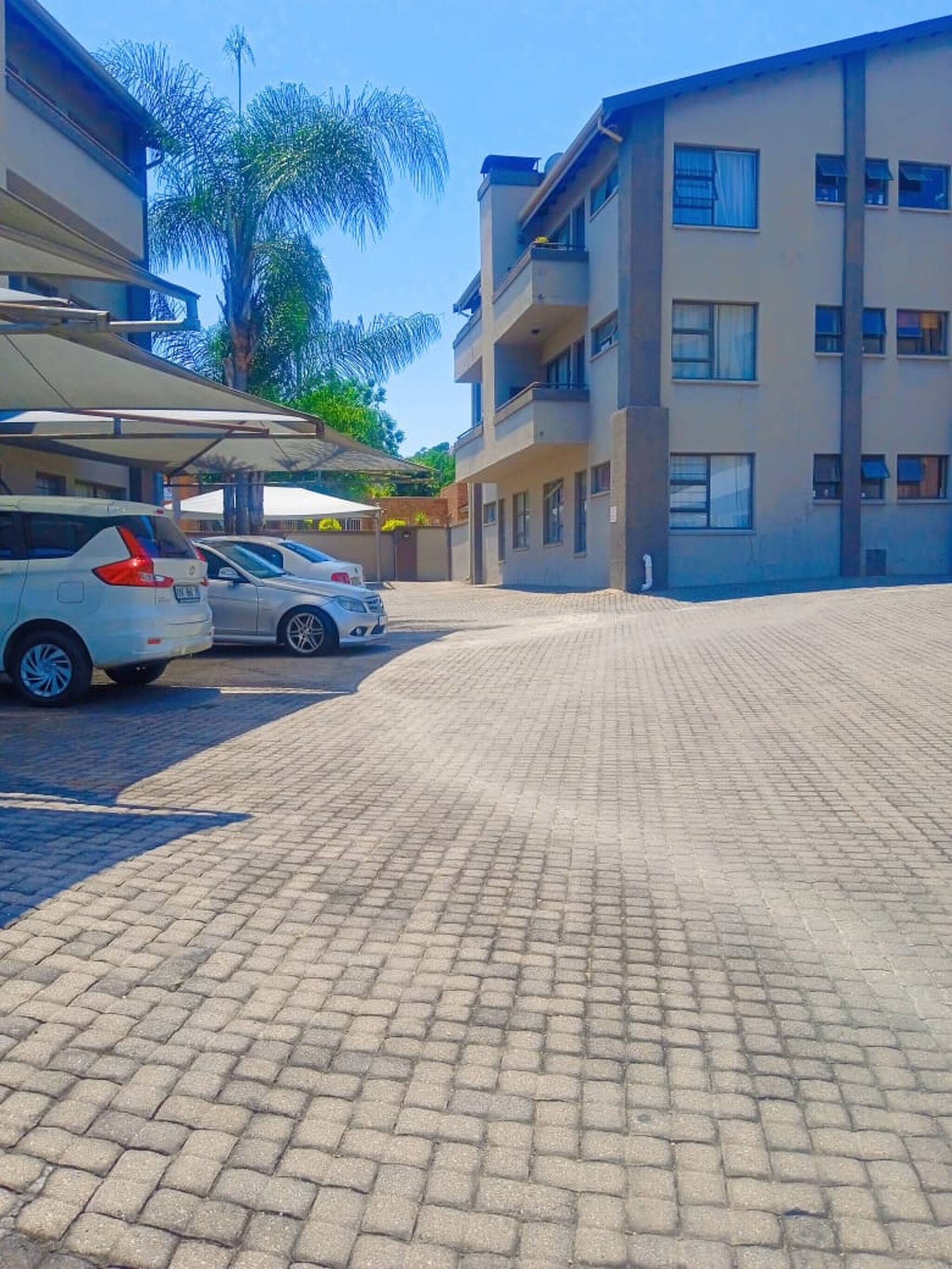 A paved courtyard with parked cars and a multi-story building with balconies.