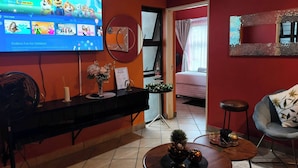 Un salon avec un téléviseur diffusant une chaîne pour enfants, une console sur laquelle est posé un vase, et un lit à l’arrière-plan.