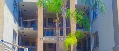 A multi-story building with balconies, a central palm tree, and a paved courtyard.