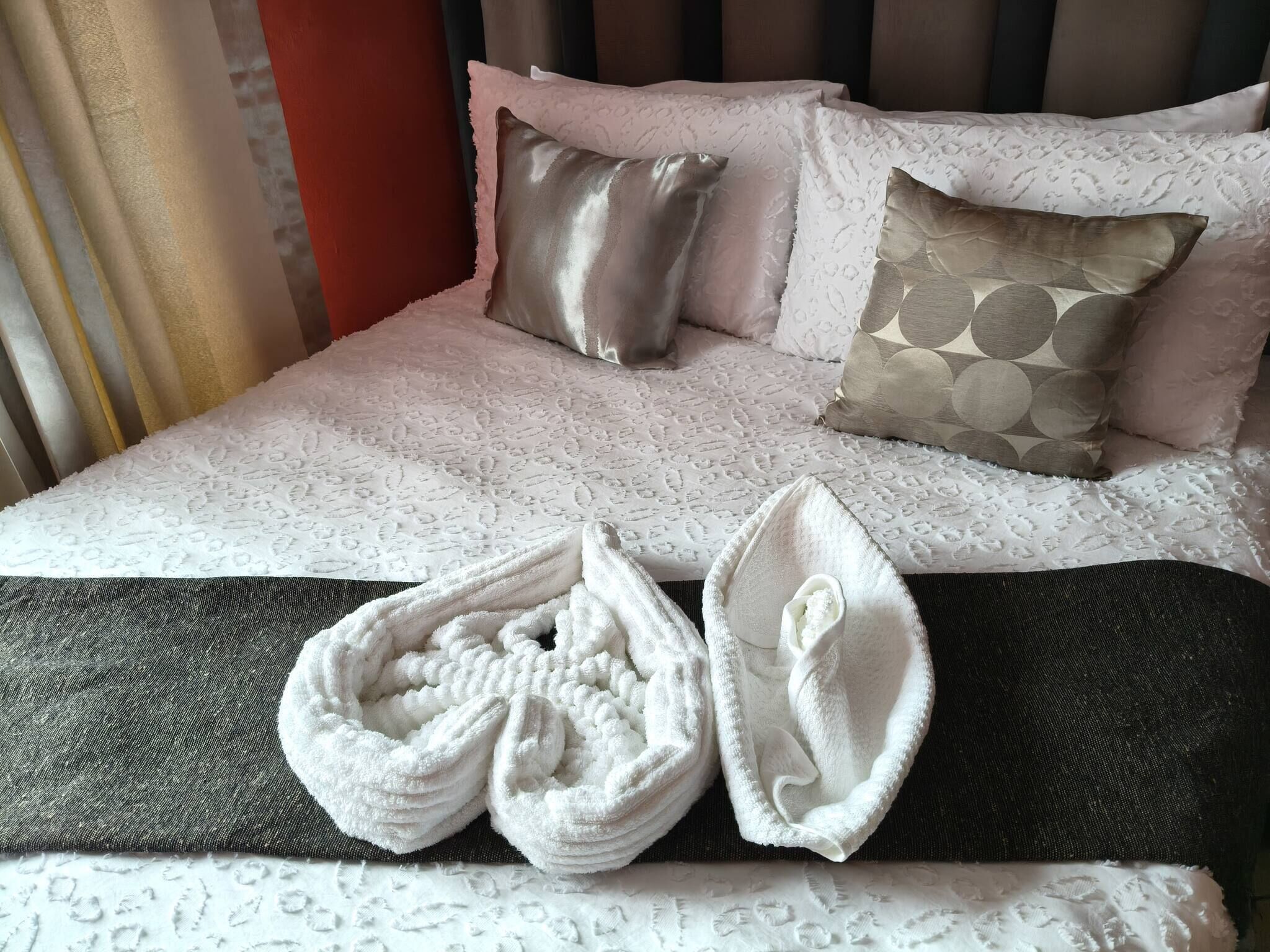 A bed with patterned bedding and a pair of white slippers.