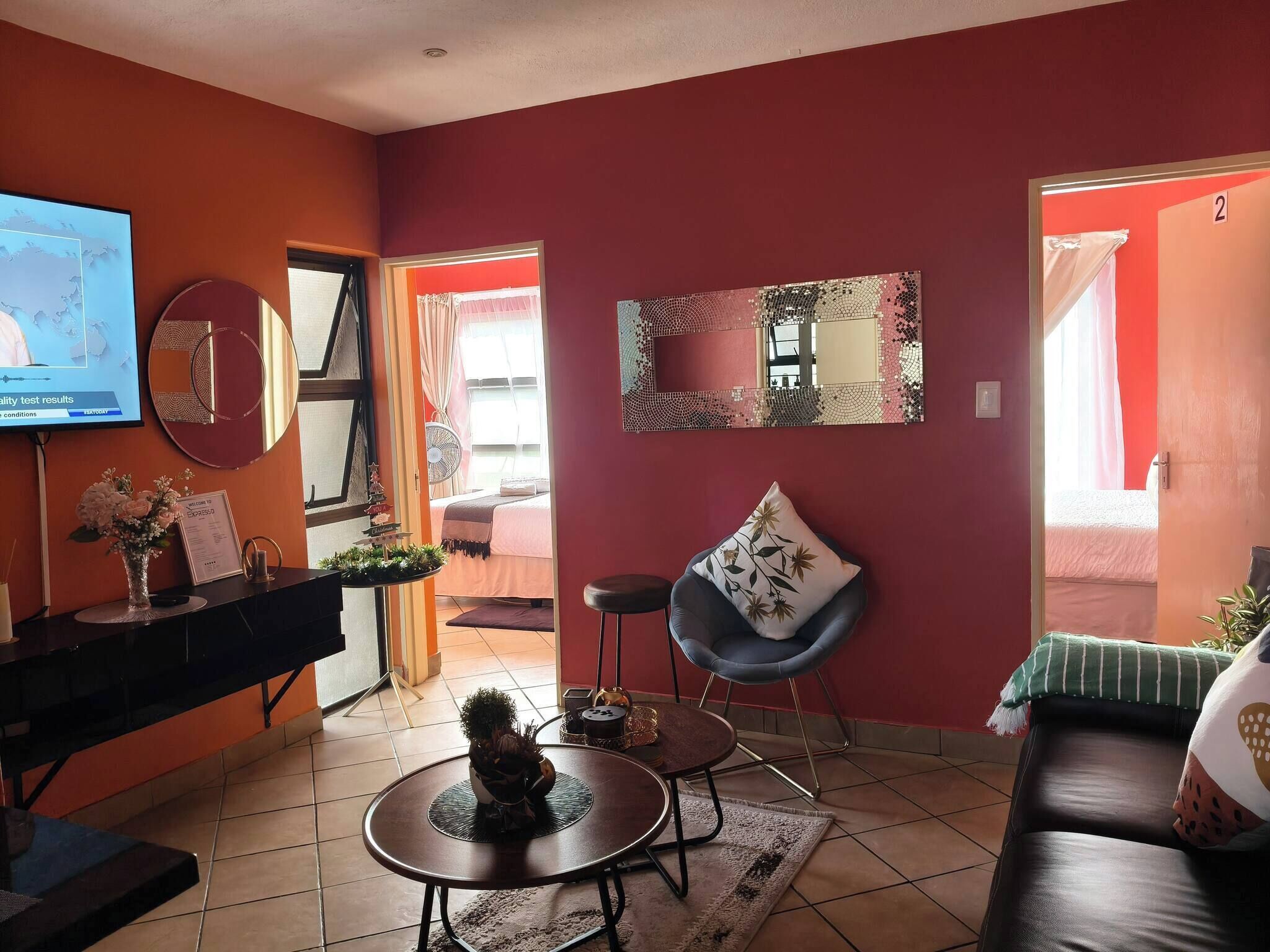 Una sala de estar con televisor, una mesa redonda de centro, un sofá de cuero negro, un espejo y una puerta que da a otra habitación.
