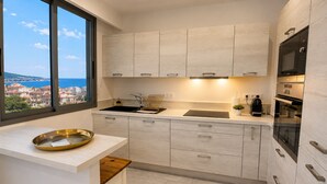 A modern kitchen with a large window, a sink, a stove, and cabinets. - 16672352 LIONS 1-Bedroom LOUIS BLANC: Elegance and Light (Cannes)