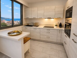 A modern kitchen with a large window, a sink, a stove, and cabinets. - 16672352 LIONS 1-Bedroom LOUIS BLANC: Elegance and Light (Cannes)