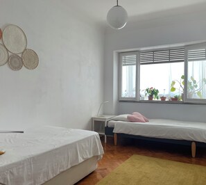 Ein Schlafzimmer mit zwei Betten, einem Fenster mit Jalousien, einem Nachttisch und einer Hängelampe.