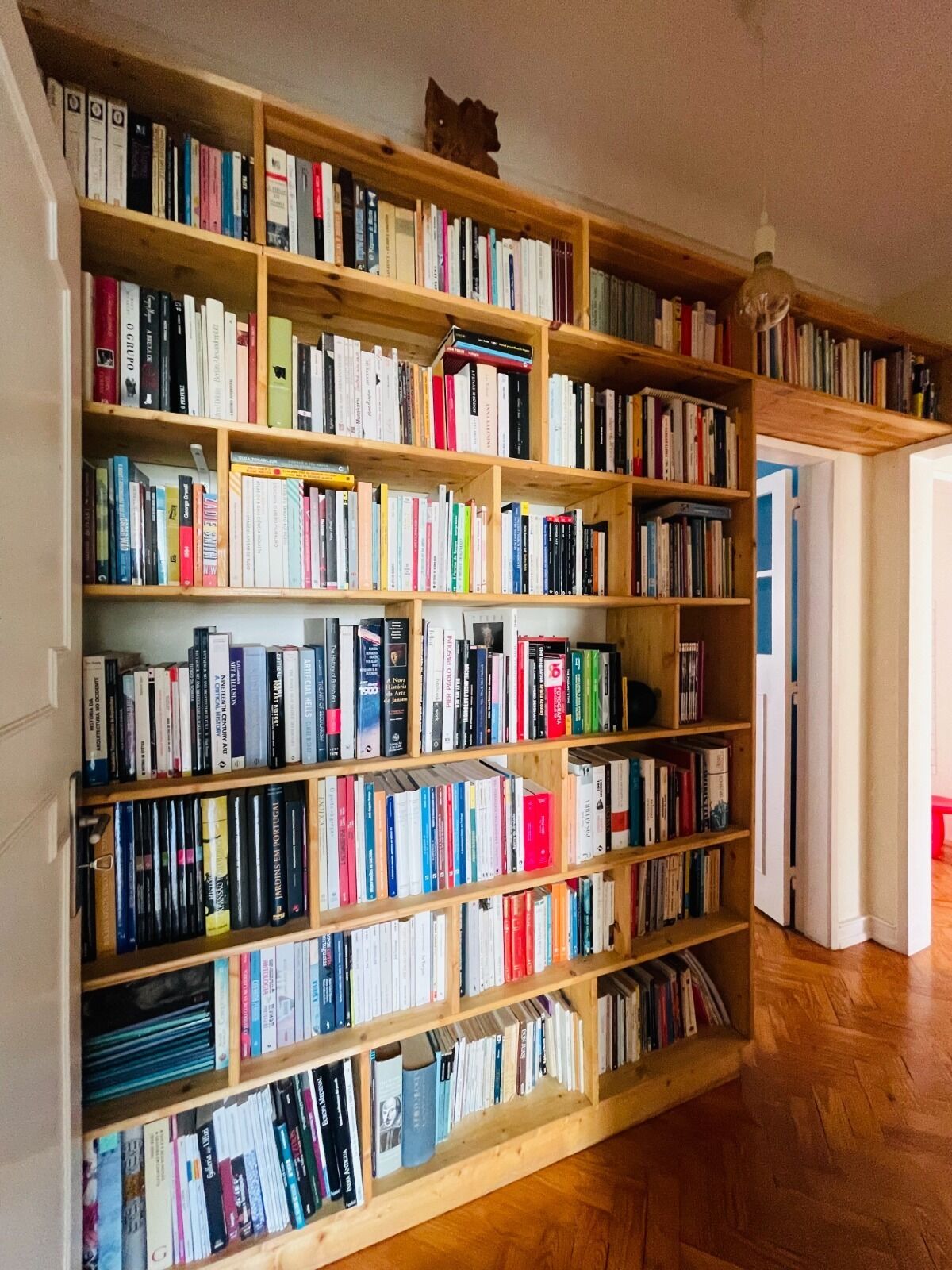 Una gran biblioteca de fusta plena de llibres, un sòl de fusta i una porta que condueix a una altra habitació.
