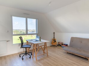A room with a large window, a desk with a laptop, a guitar, a sofa, and a radiator. - House in Saint-pabu Near Stunning Beaches (Saint-Pabu)