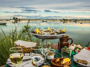 Uma mesa de jantar com ostras, copos de vinho e um jarro, com vista para um lago.