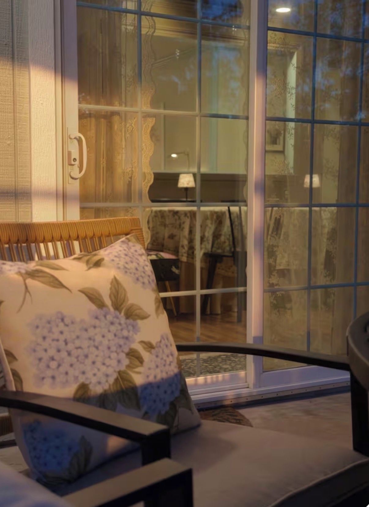 A room with a cushioned seating area, a glass door leading to an outdoor space, and a visible table with a lamp.