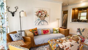 A cozy living room with a sofa, armchairs, a coffee table, and a wall-mounted deer head. - The Long Weekend Cottage Charming English Cottage Minutes from Main Street (Fredericksburg)
