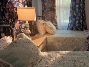 Ein Schlafzimmer mit zwei Betten, einem Nachttisch, einer Lampe und blumigen Vorhängen.