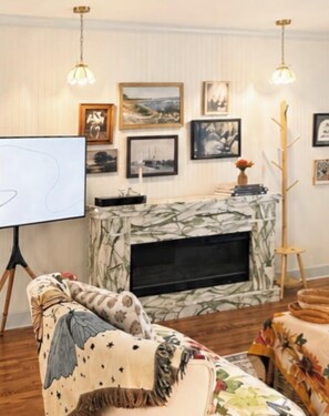 Ein Wohnzimmer mit Kamin, gerahmten Kunstwerken an der Wand und einer Whiteboard-Tafel.