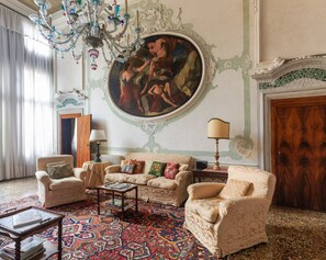 Ein Zimmer mit einem großen, verzierten Gemälde, einem Kronleuchter und einem gemusterten Teppich.