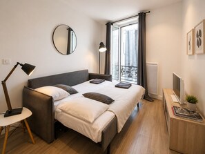 Ein modernes Schlafzimmer mit Bett, Nachttischlampe und Blick auf die Stadt durch ein Fenster.