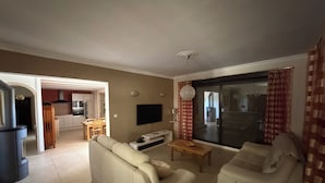 Een woonkamer met een bank, televisie en een eethoek op de achtergrond.