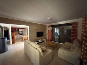 Ein Wohnzimmer mit einer Couch, einem Fernseher und einem Essbereich im Hintergrund.