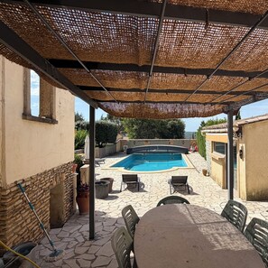 Ein überdachter Außenbereich mit Pool, Steinböden und Gartenmöbeln.