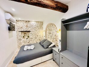 Ein Schlafzimmer mit Steinwand, einem Bett mit Kissen, einem Nachttisch, einem Kleiderschrank und einem an der Wand befestigten Fernseher.